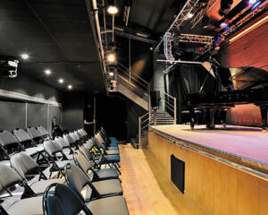 Salle 2 : parterre de salle équipé de fauteuils mobiles avec un des deux renforts de graves d&b audiotechnik intégré au centre de la paroi de la scène