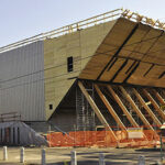 Vue du chantier. La structure en bois de la salle apparaît, soutenue par les troncs qui formeront le foyer.